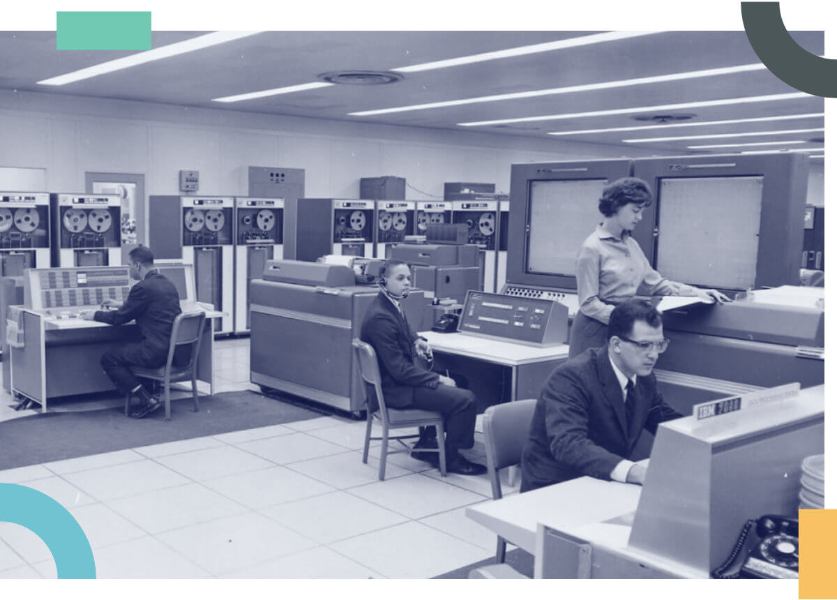 A vintage room with computers, people and tapes to illustrate how DNSimple can work for your business